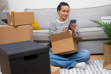 Aufkleber - Woman scrolls Internet in telephone with gearbox on lap near sofa in modern house waiting for husband to help sort out things for decoration contemporary apartment