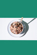 Cereal de granola muesli en un tazón blanco con cuchara sobre fondo verde. Vista superior	