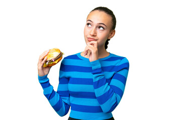 Wall Mural - Young Arab woman holding a burger over isolated background and looking up