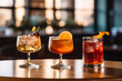Three different colored cocktails on the bar counter with ice spread around and a shallow depth of field of the bar