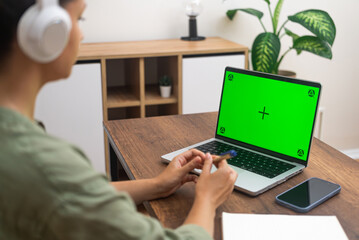 Aufkleber - Female student in headphones watches online lesson on laptop with chromakey screen woman holds pen preparing to make notes of important information sitting at home side view
