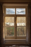 Fototapeta Na ścianę - View of the natural countryside through an old-fashioned window with net curtains on the sides.