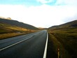 Droga asfaltowa rozciąga się pomiędzy górami. Górska droga znajdująca się na Wyspach Owczych. Surowy klimat widoczny w oddali.
