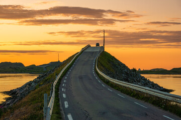 Wall Mural - A car on the Fredvang bridges in Lofoten, Norway with a beautiful sunset over the sea. Calm waters, reflections. Summer night.