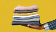 Cropped man hand holding stack of folded clothes isolated on yellow background