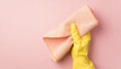 Top view of hand in yellow glove holding pastel pink rag on pink background with copy space