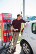 © scharfsinn86 - A man stands at the charging station and holds a plug of the charger for an electric car.