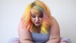 Chubby woman with rainbow hair sitting bend forward and looking down on a white background
