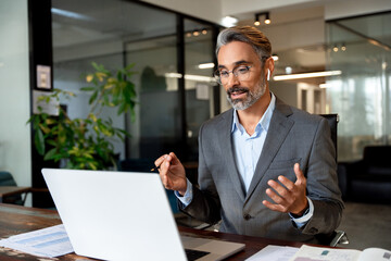 Middle-age Hispanic man using computer remote for business studying, watch online virtual webinar training meeting, video call. Smiling mature Indian or Latin businessman working on laptop in office.