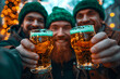 Cropped top view portrait of three men in green hat celebrating St Patrick's day, clinking glasses with alcohol beverage, drinking lager