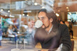 © ADDICTIVE STOCK - Through window view of thoughtful mature Latin businessman with long hair looking away while drinking coffee in a downtown cafe