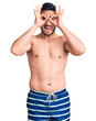 Young handsome man wearing swimwear doing ok gesture like binoculars sticking tongue out, eyes looking through fingers. crazy expression.