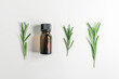 rosemary essential oil in a yellow glass bottle and rosemary sprigs on a white background, top view