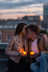 Wall Mural - Romantic beautiful surprise on Saint Valentine's Day for a girlfriend. Loving young couple having dinner on a rooftop on sunset evening with candles, wine. Skyscrapers on background, urban cityscape