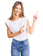 © Krakenimages.com - Beautiful caucasian woman with blonde hair wearing casual white tshirt smiling and looking at the camera pointing with two hands and fingers to the side.