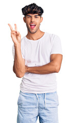 Sticker - Young hispanic man wearing casual clothes smiling with happy face winking at the camera doing victory sign. number two.