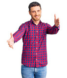 Fototapeta Natura - Handsome young man with bear wearing casual shirt looking at the camera smiling with open arms for hug. cheerful expression embracing happiness.