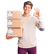 © Krakenimages.com - Young handsome man holding delivery package doing ok sign with fingers, smiling friendly gesturing excellent symbol