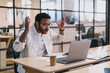 © BullRun - Anxious ethnic man with raised hands working with laptop in office