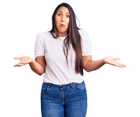 Canvas Print - Young beautiful brunette woman wearing casual t-shirt clueless and confused expression with arms and hands raised. doubt concept.