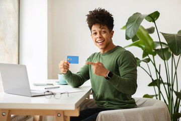 Wall Mural - Happy young black guy showing bank credit card, cafe interior