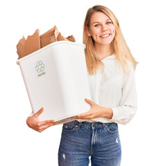 Wall Mural - Young beautiful blonde woman holding recycle paper bin looking positive and happy standing and smiling with a confident smile showing teeth