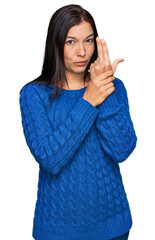 Wall Mural - Young hispanic woman wearing casual clothes holding symbolic gun with hand gesture, playing killing shooting weapons, angry face