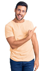 Wall Mural - Young hispanic man wearing casual clothes cheerful with a smile of face pointing with hand and finger up to the side with happy and natural expression on face