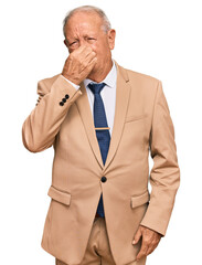 Canvas Print - Senior caucasian man wearing business suit and tie smelling something stinky and disgusting, intolerable smell, holding breath with fingers on nose. bad smell