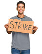 © Krakenimages.com - Young handsome african american man holding strike banner cardboard looking positive and happy standing and smiling with a confident smile showing teeth