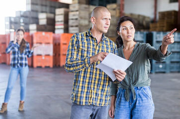 Man and woman stand inside fruit warehouse and discuss a document