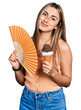 © Krakenimages.com - Hispanic young woman holding hand fan eating ice cream relaxed with serious expression on face. simple and natural looking at the camera.