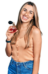 Canvas Print - Hispanic young woman holding perfume looking positive and happy standing and smiling with a confident smile showing teeth