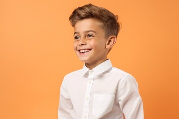 Portrait of a smiling little boy in a white shirt on an orange background