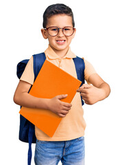 Wall Mural - Little cute boy kid wearing school bag and holding book smiling happy pointing with hand and finger