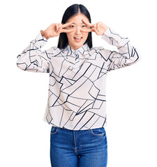 Canvas Print - Young beautiful chinese woman wearing casual shirt doing peace symbol with fingers over face, smiling cheerful showing victory