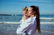 © Taras Grebinets - Authentic Caucasian woman carrying and gently hugging her little daughter, enjoying happy time together on the beach