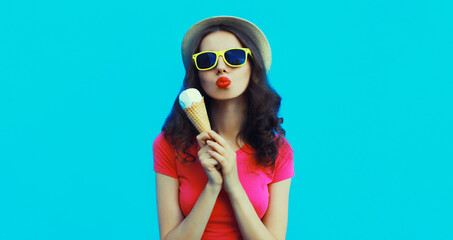 Wall Mural - Summer portrait of happy young woman eating ice cream wearing sunglasses on blue background