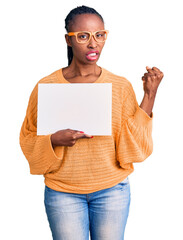 Poster - Young african american woman holding cardboard banner with blank space annoyed and frustrated shouting with anger, yelling crazy with anger and hand raised