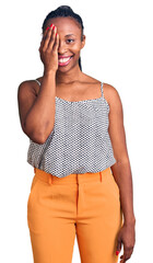 Sticker - Young african american woman wearing casual clothes covering one eye with hand, confident smile on face and surprise emotion.