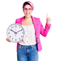 Sticker - Young beautiful woman with pink hair wearing business jacket and holding clock surprised with an idea or question pointing finger with happy face, number one