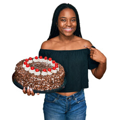 Poster - Young african american woman celebrating birthday holding big chocolate cake pointing finger to one self smiling happy and proud