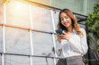 © sorapop - Asian businesswoman holding mobile phone texting message outside of office, Happy young woman using smartphone outdoor on urban city street, applications on cell phone, checking social media