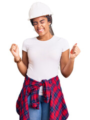 Sticker - Young african american woman with braids wearing hardhat and builder clothes very happy and excited doing winner gesture with arms raised, smiling and screaming for success. celebration concept.