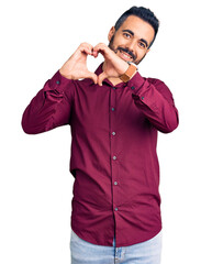 Sticker - Young hispanic man wearing casual clothes smiling in love showing heart symbol and shape with hands. romantic concept.