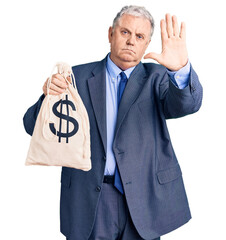 Sticker - Senior grey-haired man wearing business suit holding money bag with dollar symbol with open hand doing stop sign with serious and confident expression, defense gesture