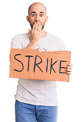 Wall Mural - Young handsome man holding strike banner covering mouth with hand, shocked and afraid for mistake. surprised expression