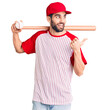 © Krakenimages.com - Young handsome man with beard playing baseball holding bat and ball pointing thumb up to the side smiling happy with open mouth