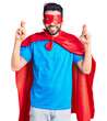© Krakenimages.com - Young handsome man with beard wearing super hero costume gesturing finger crossed smiling with hope and eyes closed. luck and superstitious concept.