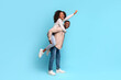 Exuberant black couple with woman on man's back, blue backdrop